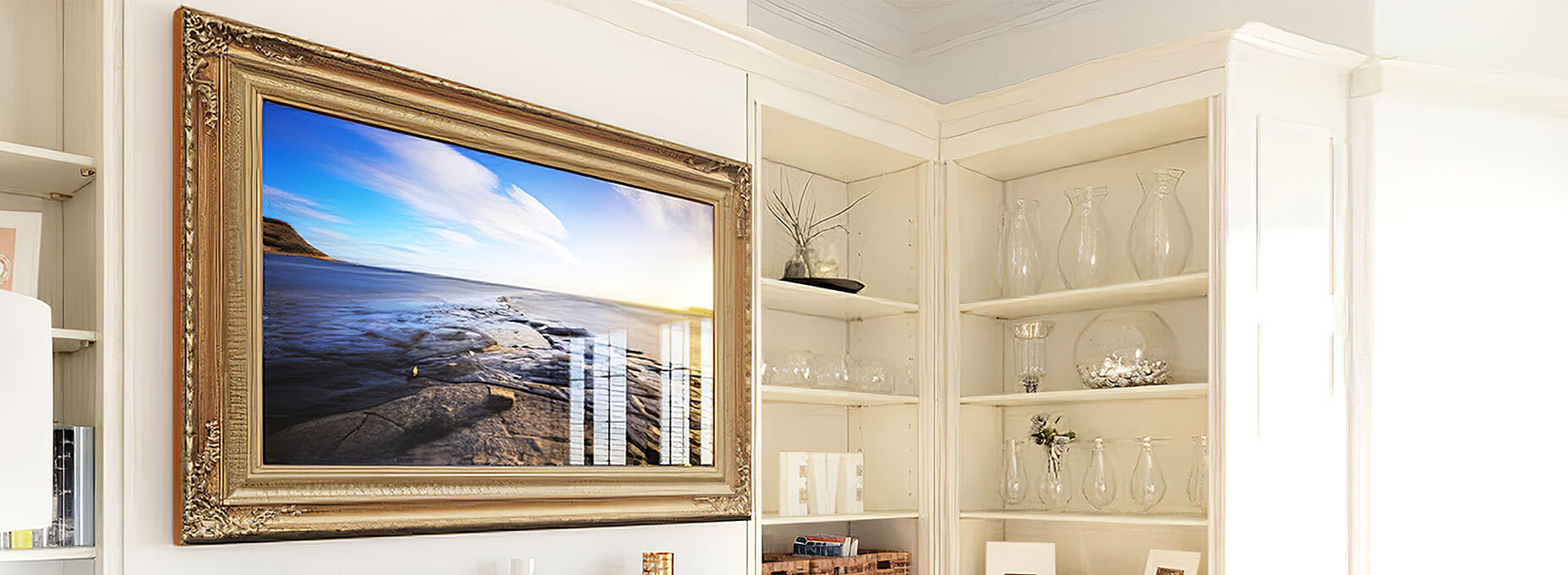 A smart TV framed in gold with classic and intricate designs on four corners attached to a wall in white room.